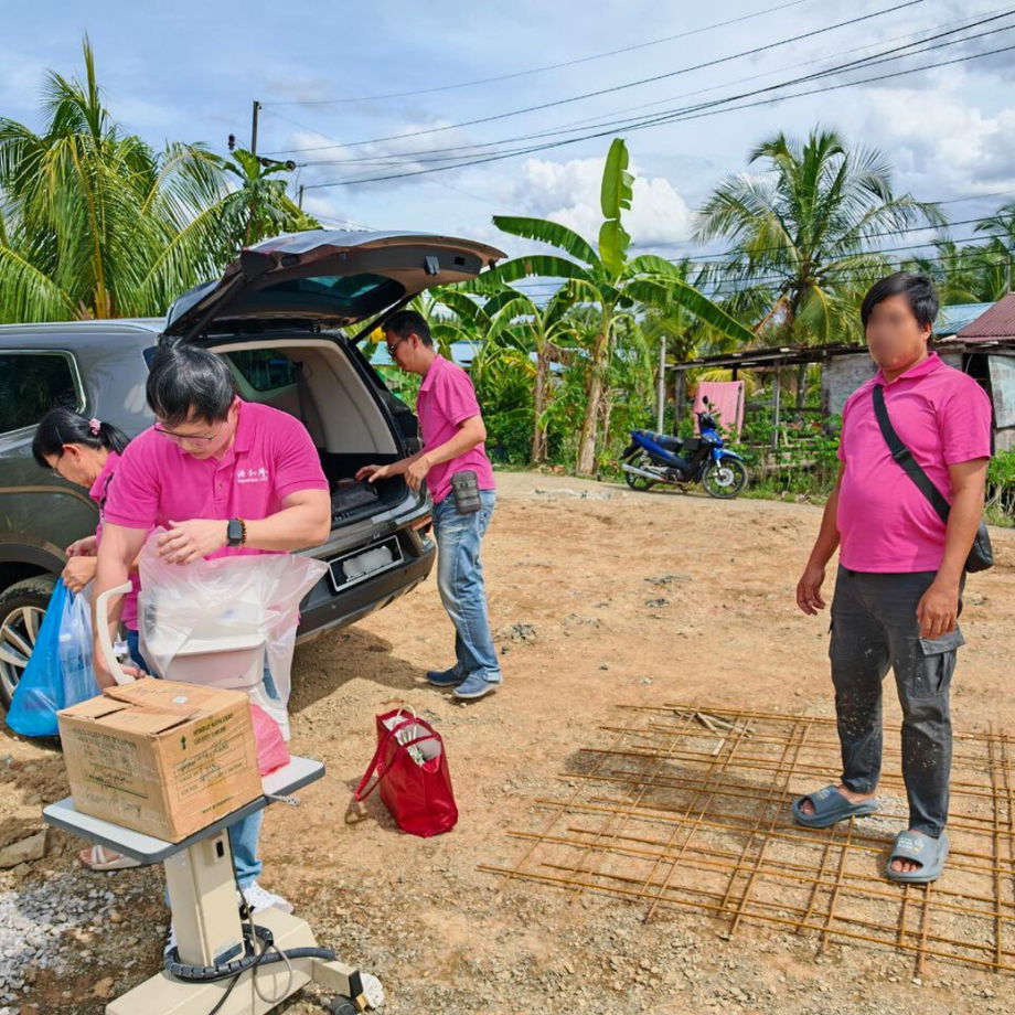 GHL VisionFirst team carrying optical equipment through muddy road and raised timber walkway at SK Muhibbah